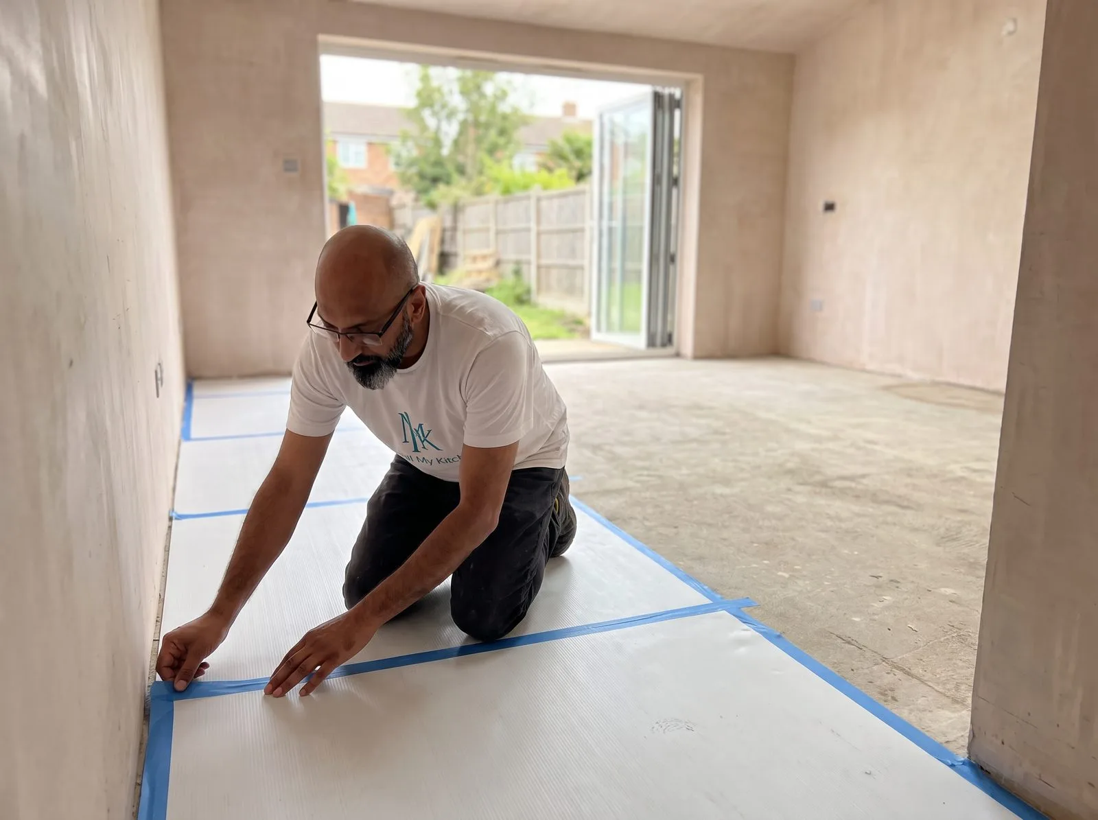Kitchen fitter laying protective correx floor sheeting along a hallway leading into the kitchen