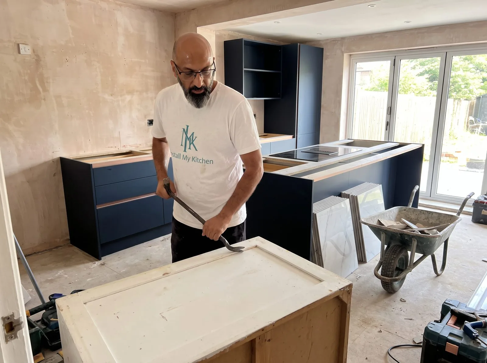 Kitchen fitter removing an old kitchen unit during strip-out, room stripped back to bare subfloor
