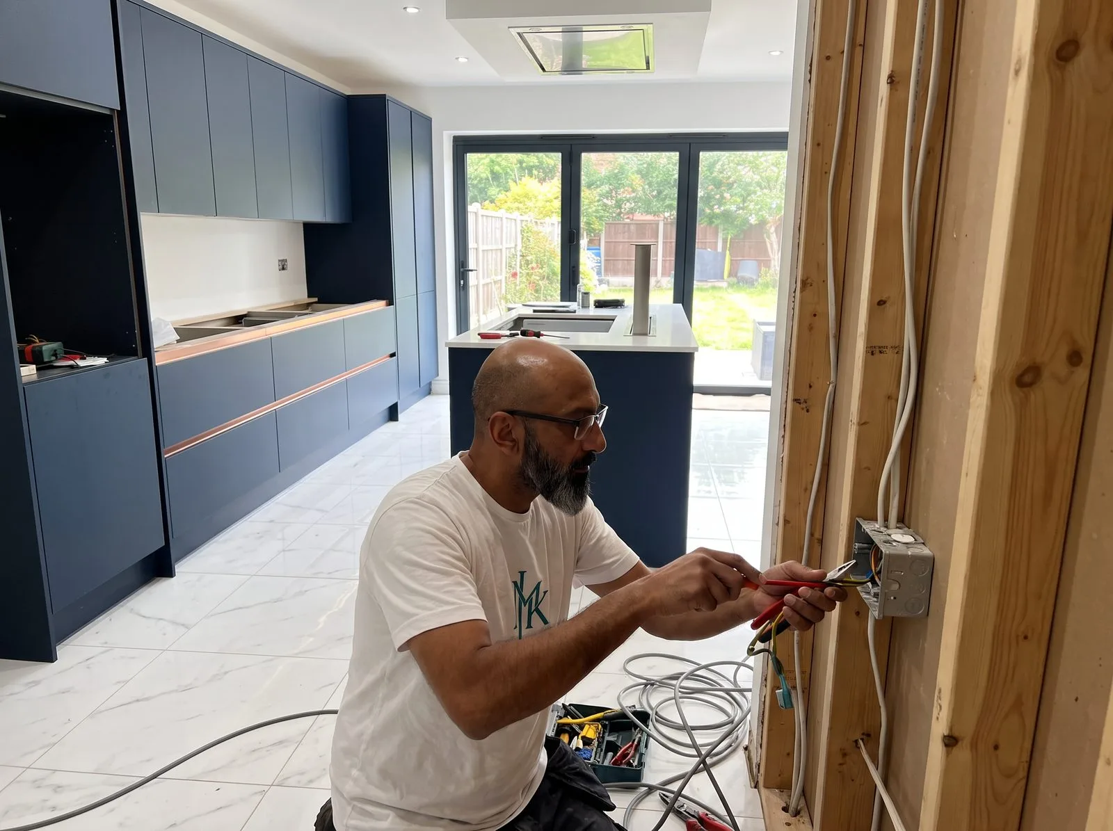Kitchen fitter wiring an electrical back box in an exposed stud wall during first fix, before plastering