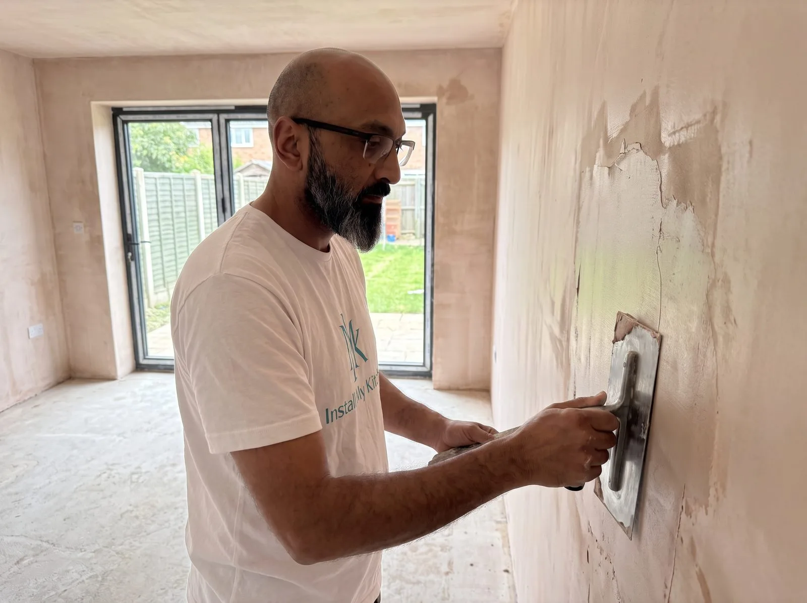 Kitchen fitter applying a plaster skim coat to a patched wall with a trowel, empty room