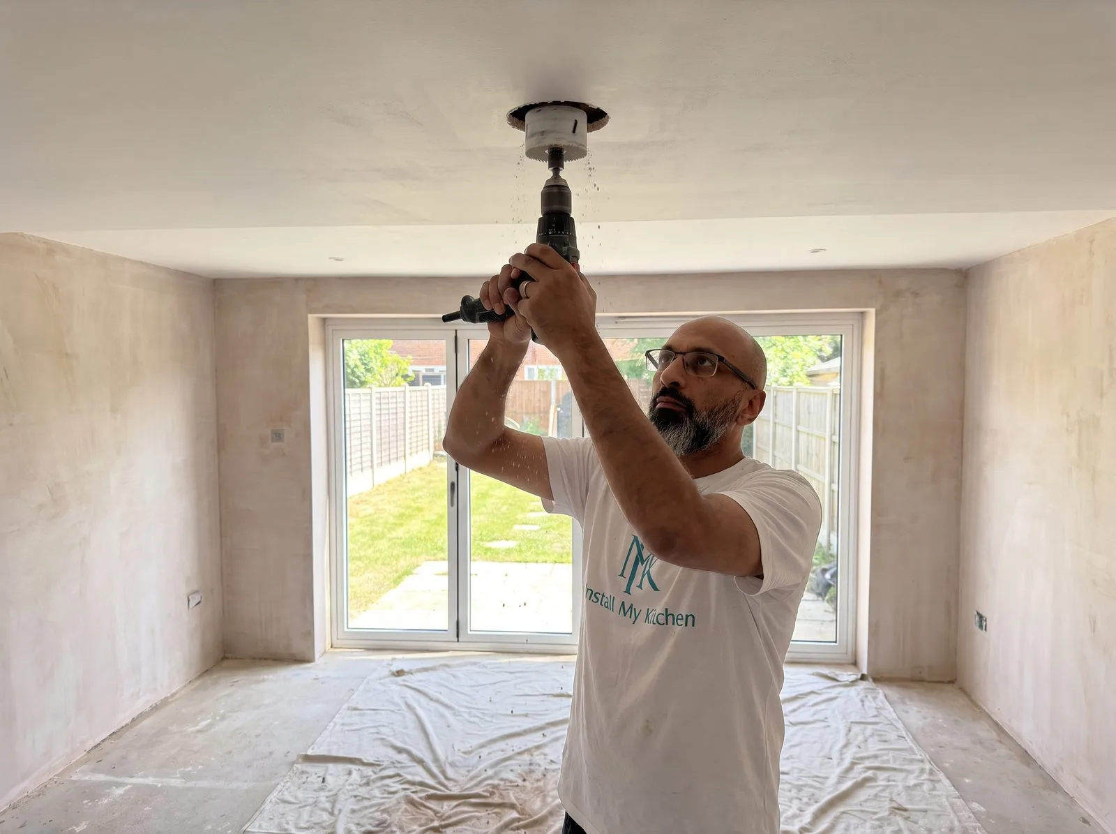 Kitchen fitter cutting a spotlight hole in the ceiling with a holesaw, empty painted room