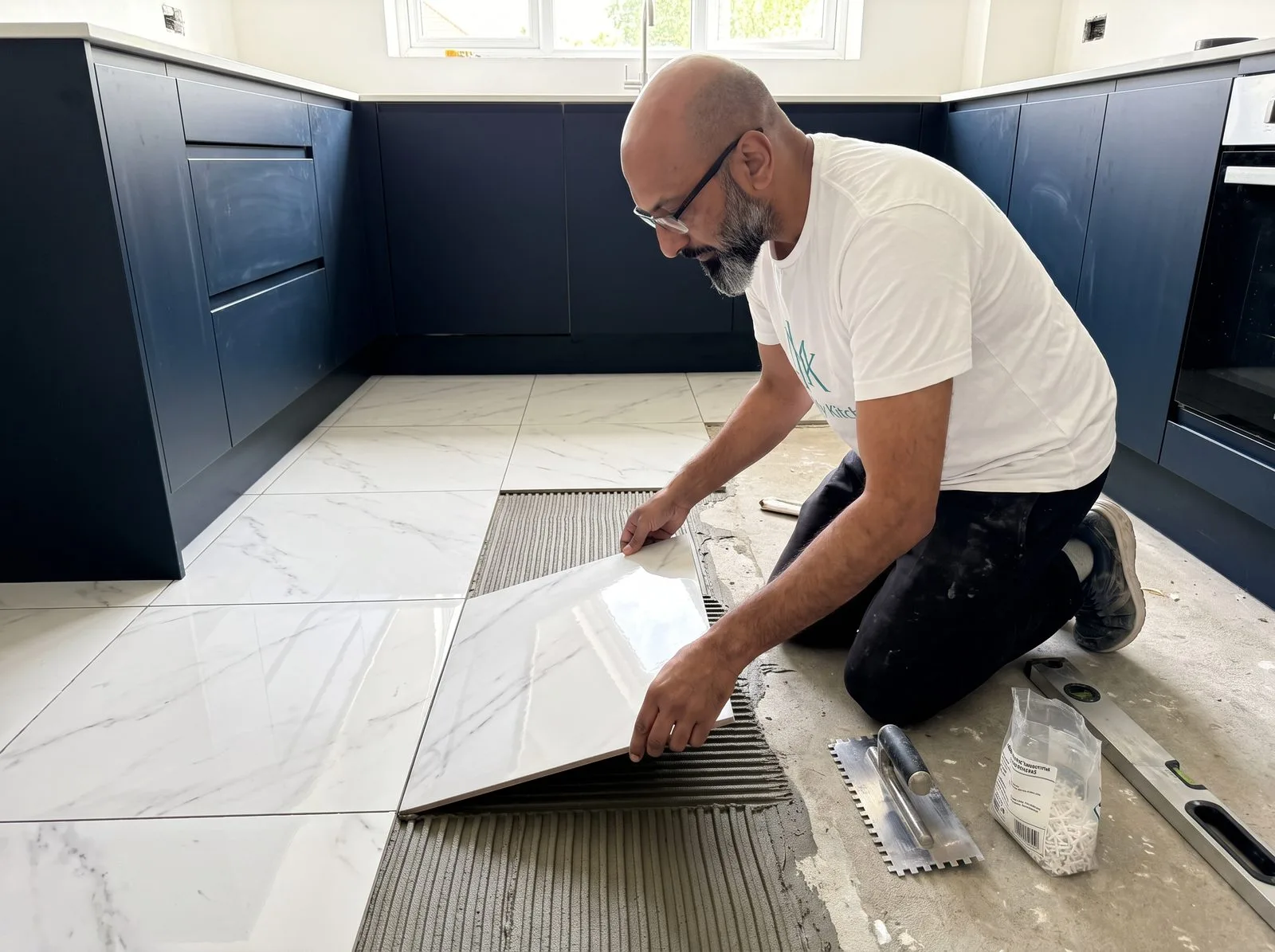 Kitchen fitter laying a large-format Carrara-white floor tile with spirit level and tile spacers