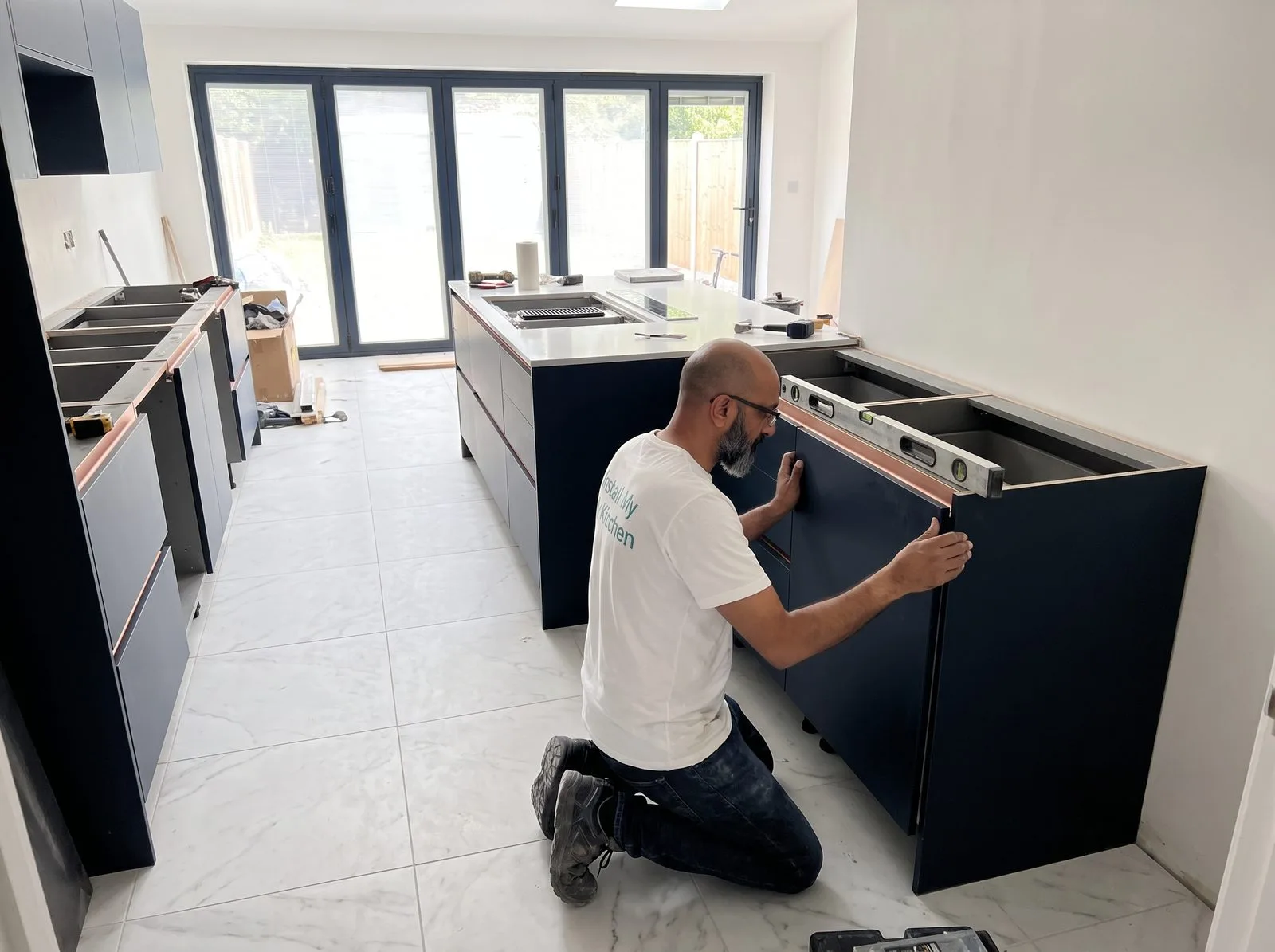 Kitchen fitter levelling a dark blue base cabinet carcass with a spirit level during perimeter installation