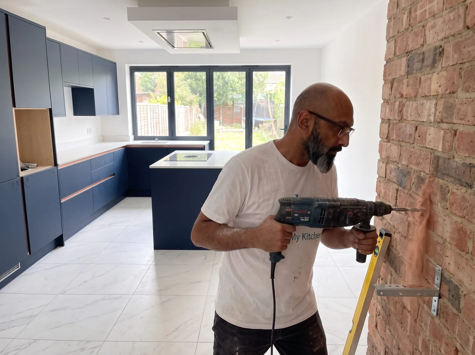 Kitchen fitter drilling into a brick wall with an SDS drill to fix a wall cabinet bracket