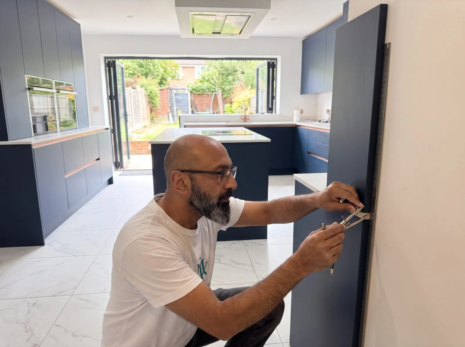 Kitchen fitter running a scribing compass down a tall end panel against an uneven wall