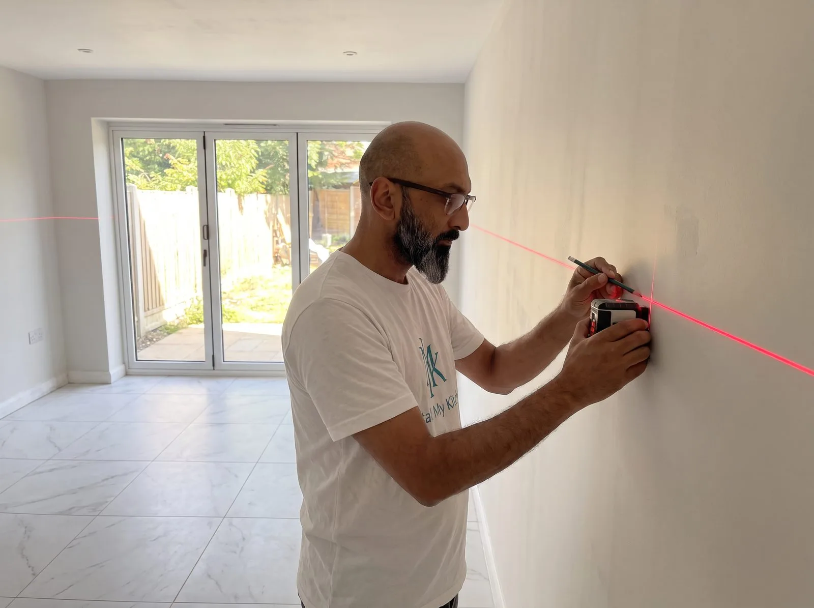 Kitchen fitter marking the 880mm datum line around an empty tiled room with a laser level