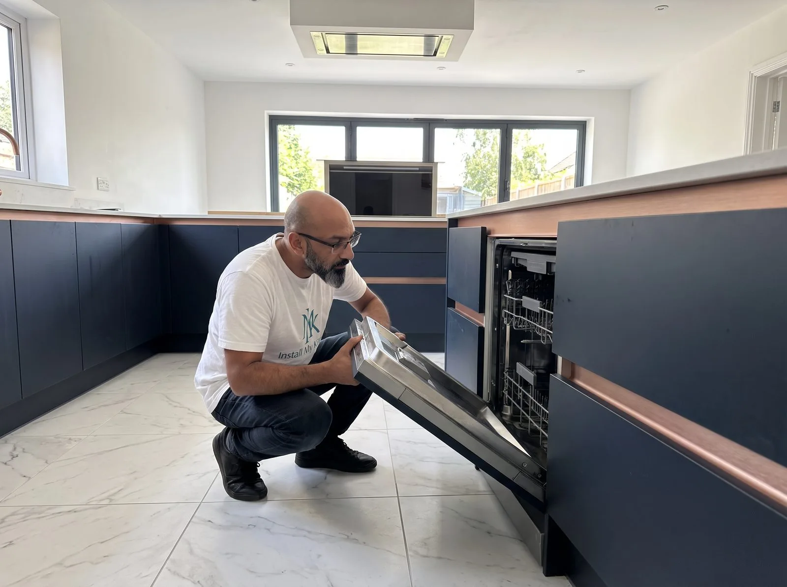 Kitchen fitter sliding an integrated dishwasher into its housing and checking alignment with cabinet fronts