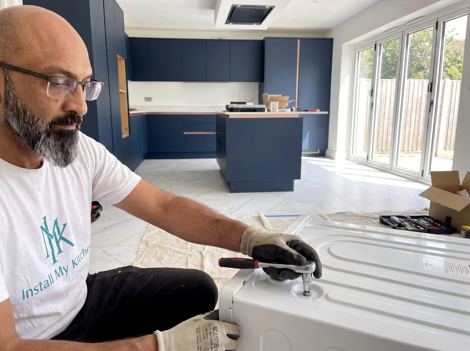 Kitchen fitter removing a transit bolt from the back of a washing machine with a socket wrench
