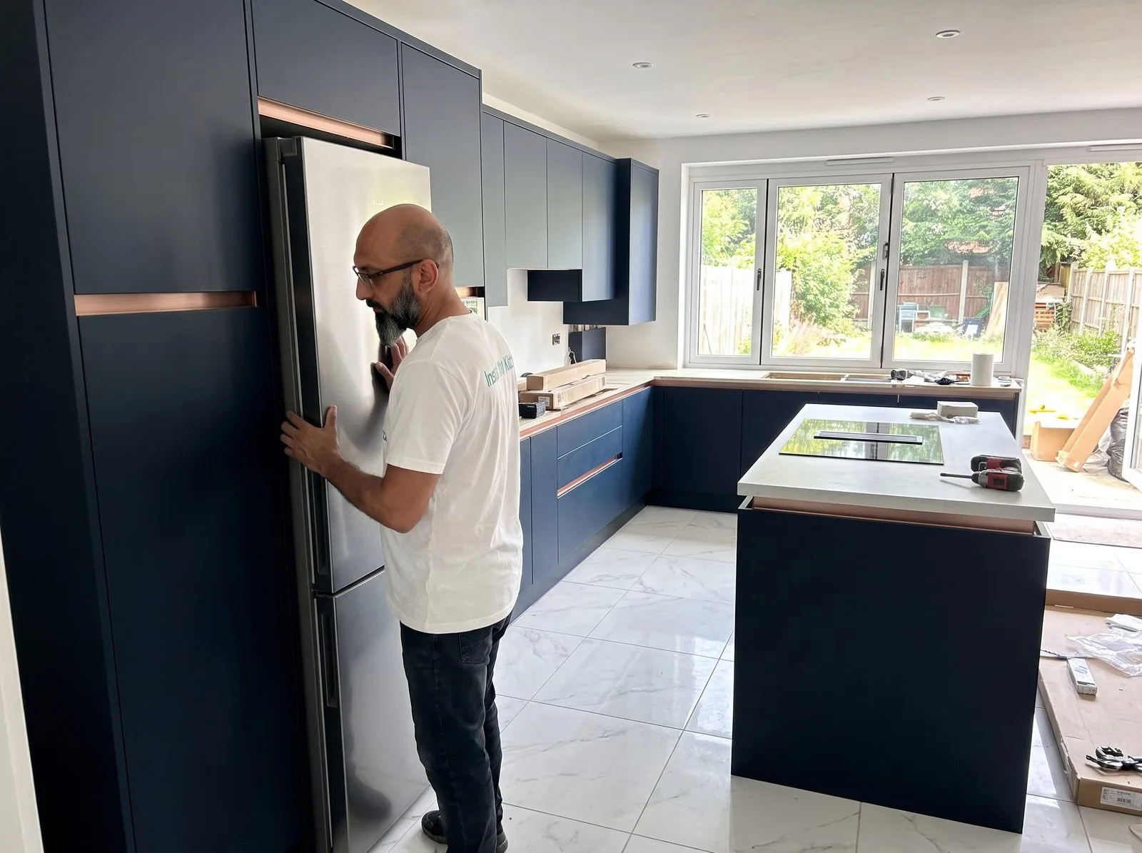 Kitchen fitter sliding an integrated fridge freezer into its tall cabinet housing
