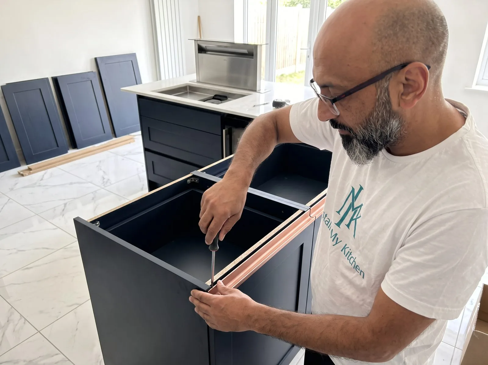 Kitchen fitter fitting a rose gold recessed handleless rail to a dark blue cabinet door