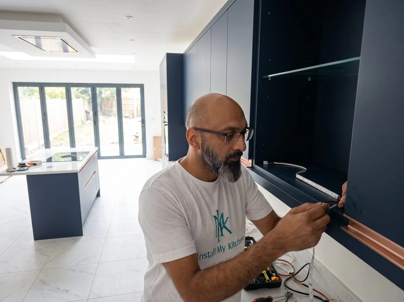Kitchen fitter wiring an LED light strip inside a glass-fronted wall cabinet